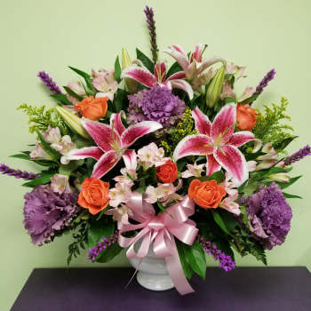 Bouquet of pink lilies, orange roses, and purple flowers in a white vase