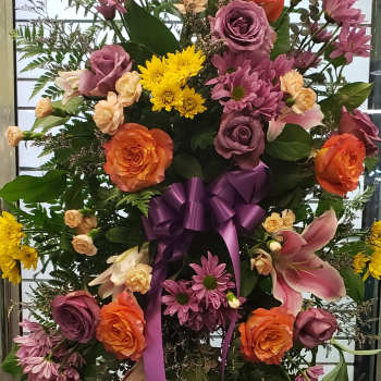 Large standing floral spray with roses, lilies, and chrysanthemums tied with a purple ribbon