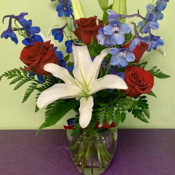 Bouquet of red roses, white lilies, and blue flowers in a glass vase
