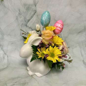 White bunny vase with yellow daisies, peach roses, and pastel decorative egg picks.