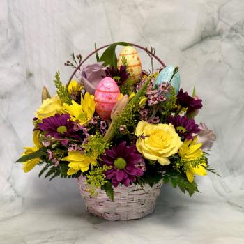 Basket arrangement of yellow and purple flowers with decorative Easter eggs