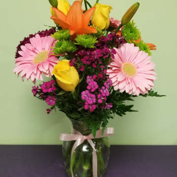 Bouquet of pink gerbera daisies, yellow roses, and orange lilies in a glass vase