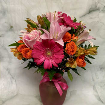 Pink and orange mixed flower arrangement in a vase with a ribbon