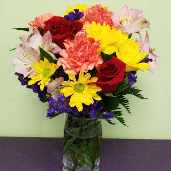Mixed bouquet of red roses, yellow daisies, pink alstroemeria, and carnations in a glass vase