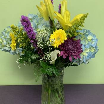 Mixed bouquet in a glass vase with blue hydrangeas, yellow lilies, and purple chrysanthemums