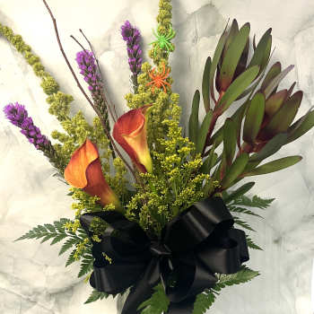 Bouquet of orange calla lilies and purple spikes in a glass vase with a black ribbon