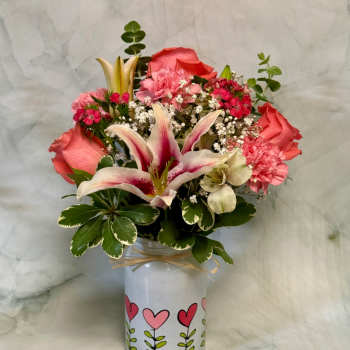Pink lilies, roses, and carnations arranged in a white vase with heart designs