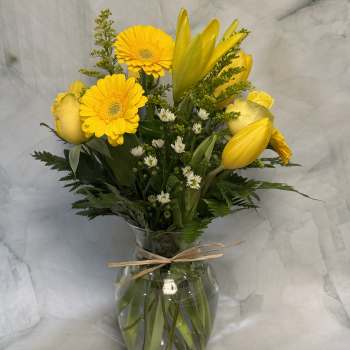 Yellow flowers arranged in a clear glass vase with a ribbon tie.