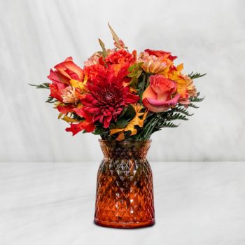 Autumn bouquet of red and orange flowers in an amber glass vase