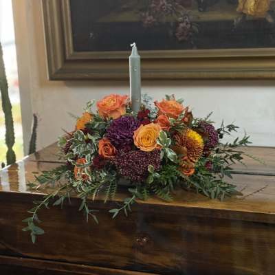 Low floral centerpiece with orange, yellow, and purple blooms around a candle