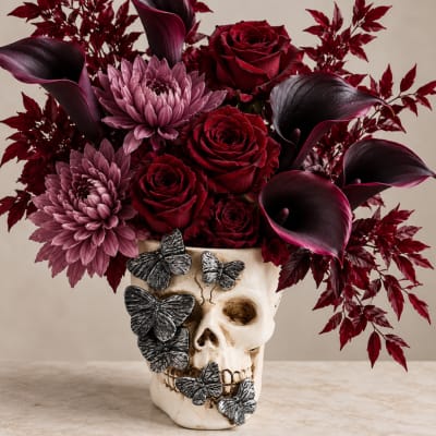 Red roses and purple flowers in a skull vase with butterfly accents