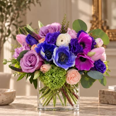 Colorful bouquet of roses, tulips, and anemones in a clear glass vase
