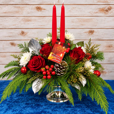Holiday centerpiece with red candles, roses, and white daisies in a silver vase
