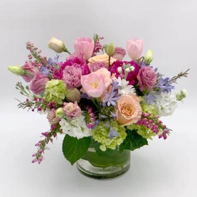 Low glass vase arrangement with pink tulips, roses, hydrangeas, and other pastel flowers