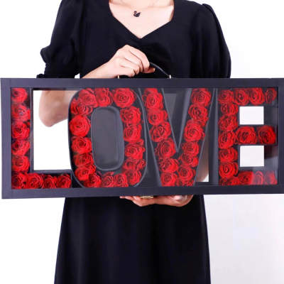 Framed LOVE sign filled with red roses, held by a person in black