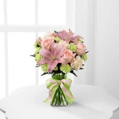 Pink lilies and roses in a glass vase with a ribbon bow