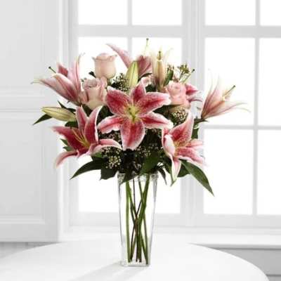 Pink lilies and roses arranged in a clear glass vase