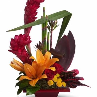 Tropical floral arrangement with orange lilies and red blooms in a red container
