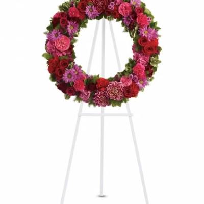 Circular floral wreath on a white easel with pink and red flowers
