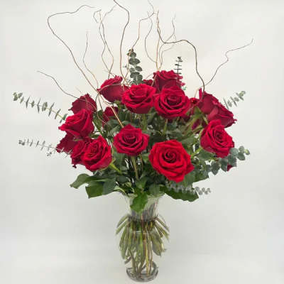 Tall arrangement of long-stemmed red roses with curly branches in a clear glass vase