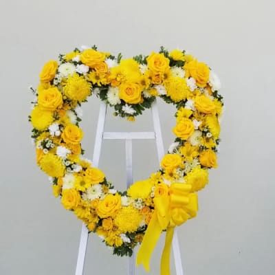 Heart-shaped yellow and white floral standing wreath with bow on a white easel