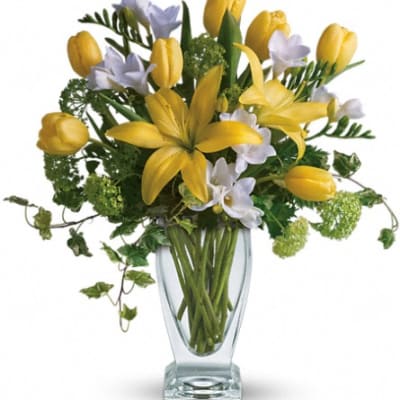 Yellow tulips and white flowers in a clear glass vase