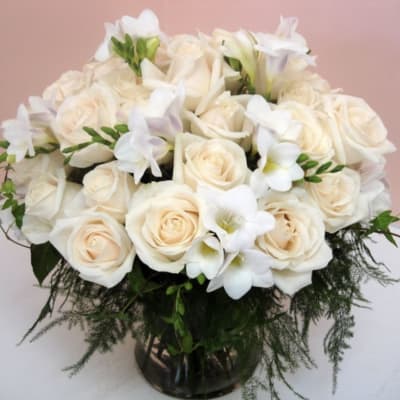 Cream roses and white flowers arranged in a glass vase