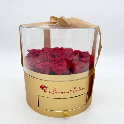 Red roses in a clear round gift box with a gold ribbon