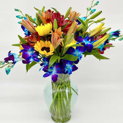 Colorful bouquet of lilies, sunflowers, and blue orchids in a glass vase