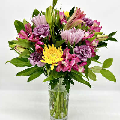 Mixed pink, purple, and yellow flowers in a clear glass vase
