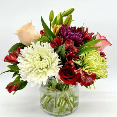 Mixed bouquet of roses, chrysanthemums, and lilies in a glass vase