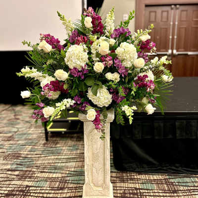 Large floral arrangement with white roses, hydrangeas, and purple blooms on a pedestal.