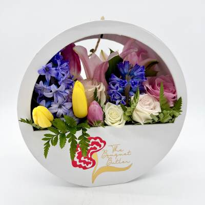 Round box arrangement with pink, yellow, and blue flowers