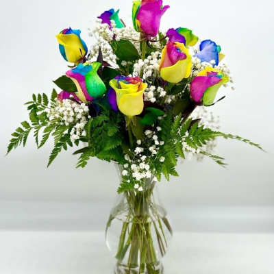 Rainbow-colored roses in a clear glass vase with baby's breath