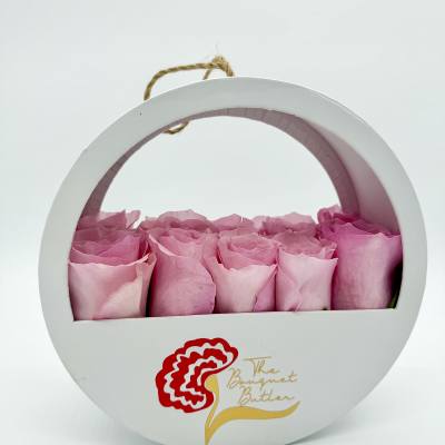 Pink roses arranged in a round white gift box with a rope handle