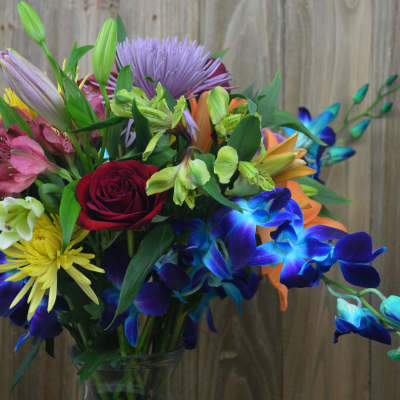 Colorful mixed bouquet with roses, lilies, and orchids in a glass vase