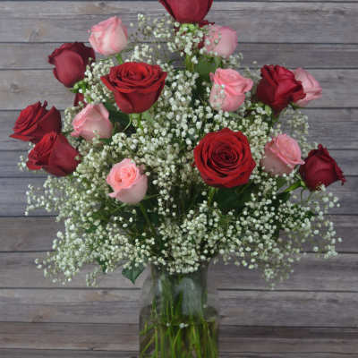 Red and pink roses arranged in a glass vase with baby's breath