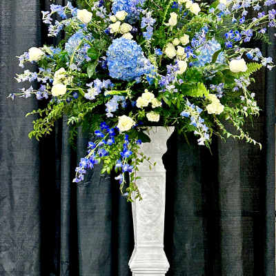 Tall blue and white floral arrangement in a white pedestal vase