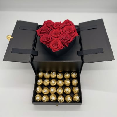 Black gift box with red roses on top and gold-wrapped chocolates below