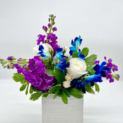 Purple and blue flowers with white roses in a white box