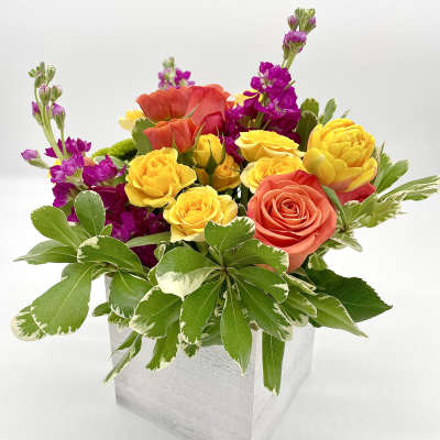 Colorful bouquet of yellow, coral, and purple flowers in a white box
