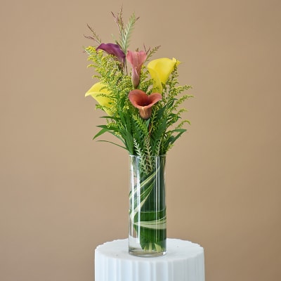 Tall vase arrangement with colorful calla lilies and greenery