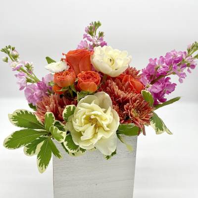 Mixed bouquet of orange, cream, and pink flowers in a white box