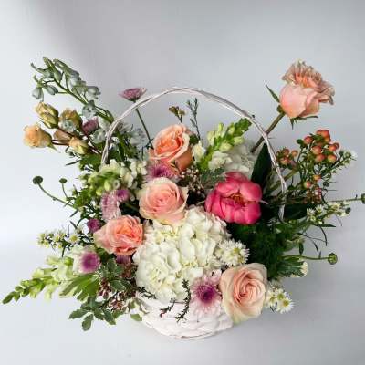 Basket arrangement of peach roses, white hydrangea, and mixed blooms