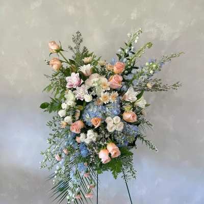 Tall standing floral spray with pastel roses, blue blooms, and white flowers