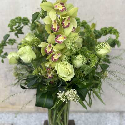 Tall green orchid arrangement in a glass vase with mixed foliage