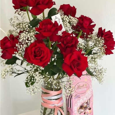 Bouquet of red roses with baby's breath in a glass vase beside a pink candy box