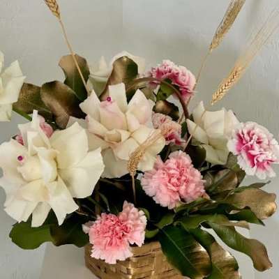 Pink and white floral arrangement in a woven basket with wheat stems