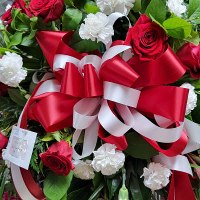 Standing floral spray with red roses, white carnations, and a red-and-white ribbon bow