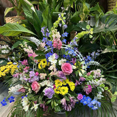 Large mixed floral arrangement with pink roses, yellow daisies, and blue delphinium